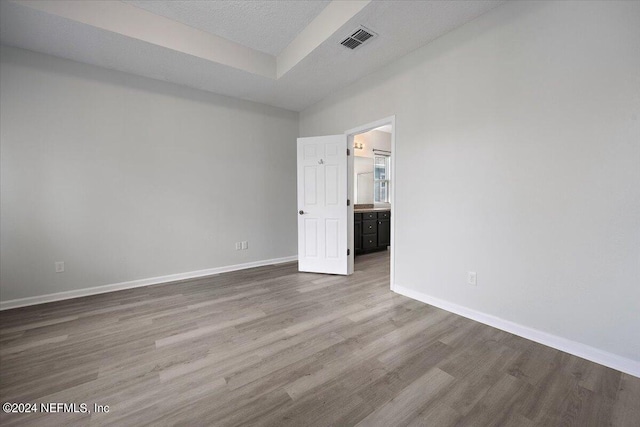 unfurnished bedroom featuring ensuite bath, a textured ceiling, and wood-type flooring