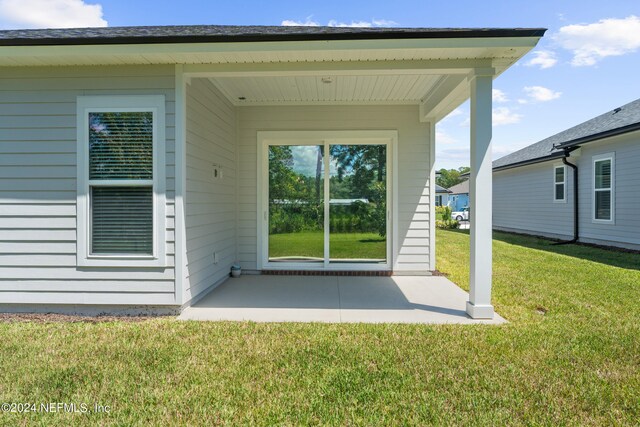 view of exterior entry with a yard and a patio