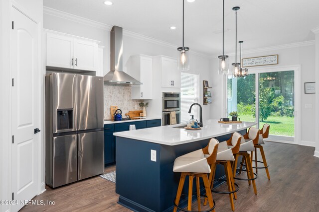 kitchen featuring hanging light fixtures, stainless steel appliances, sink, wall chimney range hood, and a breakfast bar