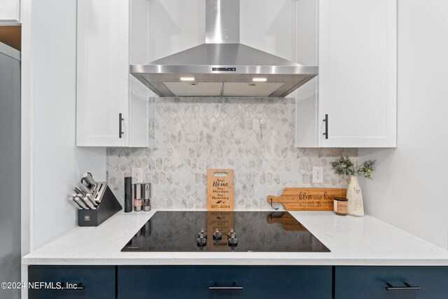 kitchen featuring black electric cooktop, tasteful backsplash, light stone counters, and wall chimney range hood