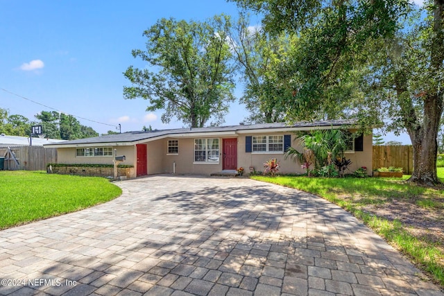 ranch-style house with a front lawn, decorative driveway, fence, and stucco siding