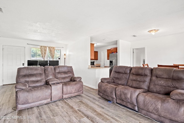 living room with a textured ceiling, light wood finished floors, visible vents, and baseboards