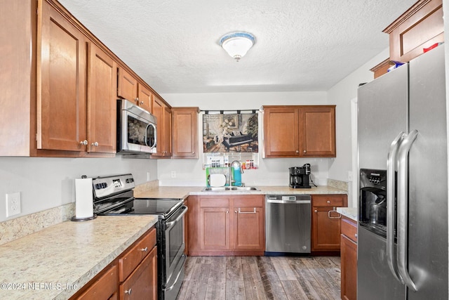 kitchen featuring stainless steel appliances, light wood finished floors, a sink, and brown cabinets