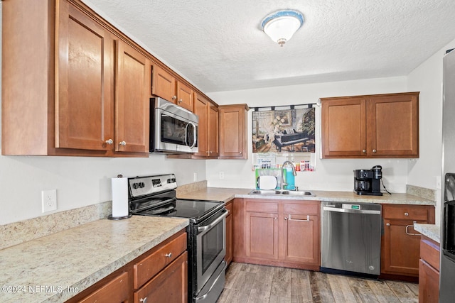 kitchen featuring light wood finished floors, light countertops, appliances with stainless steel finishes, brown cabinetry, and a sink