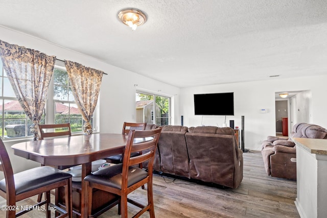 dining space featuring a textured ceiling, light wood finished floors, and baseboards