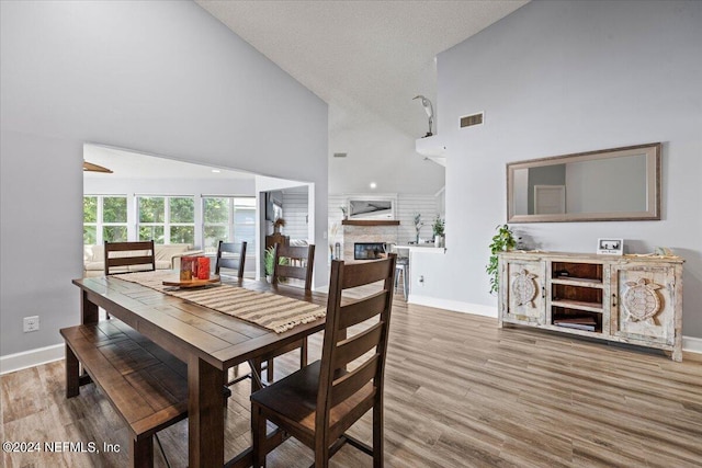 dining area with high vaulted ceiling, light hardwood / wood-style floors, and a textured ceiling