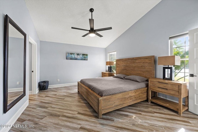 bedroom with high vaulted ceiling, ceiling fan, light hardwood / wood-style floors, and a textured ceiling