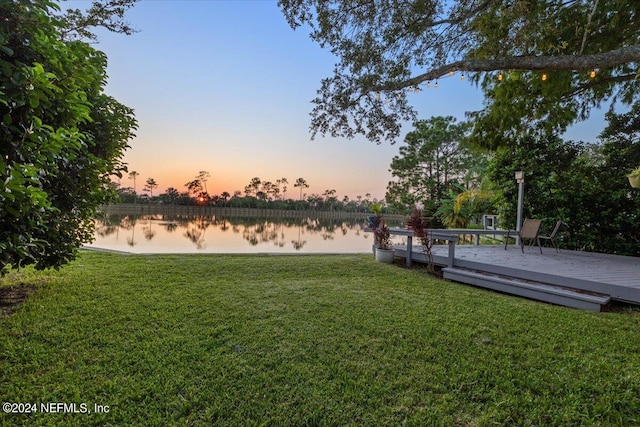 yard at dusk featuring a deck with water view