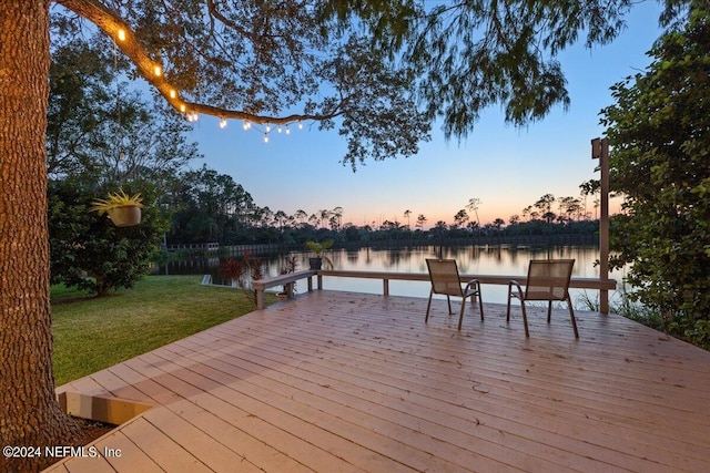 deck at dusk featuring a lawn and a water view