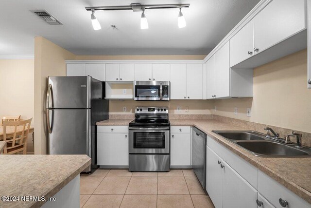 kitchen with light tile patterned floors, ornamental molding, sink, white cabinetry, and stainless steel appliances