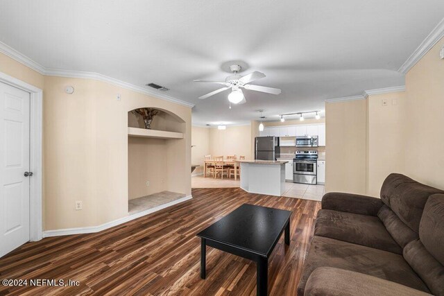 living room with ceiling fan, built in features, track lighting, ornamental molding, and hardwood / wood-style floors