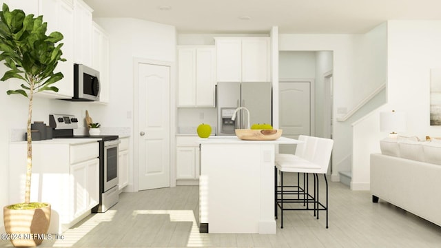 kitchen with appliances with stainless steel finishes, an island with sink, white cabinetry, and a breakfast bar