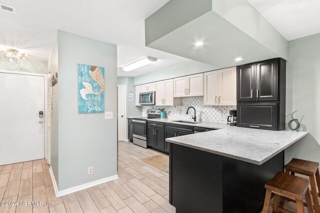 kitchen featuring light hardwood / wood-style flooring, stainless steel appliances, sink, kitchen peninsula, and a kitchen bar