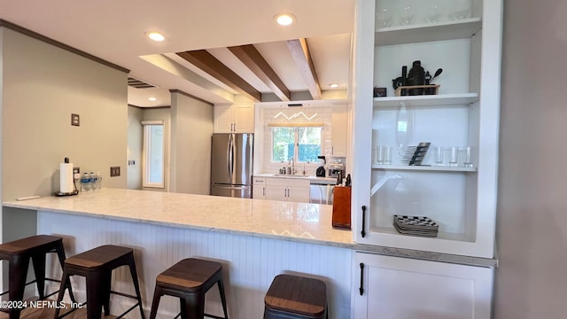 kitchen featuring light stone counters, sink, white cabinetry, stainless steel appliances, and a kitchen bar