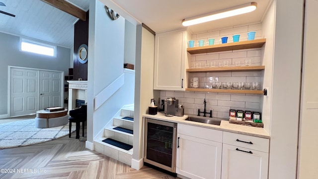 bar featuring sink, beverage cooler, white cabinets, decorative backsplash, and light parquet flooring