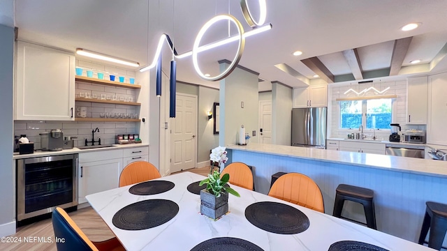 dining area with beam ceiling, wine cooler, light hardwood / wood-style floors, and sink