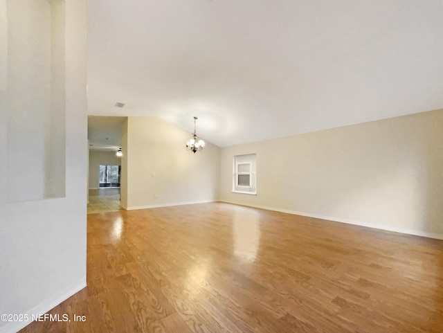 empty room featuring an inviting chandelier, baseboards, light wood finished floors, and vaulted ceiling