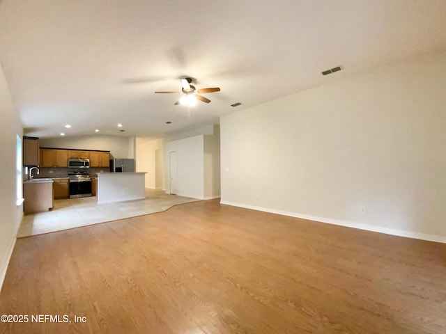 unfurnished living room featuring baseboards, lofted ceiling, light wood-style floors, a ceiling fan, and a sink