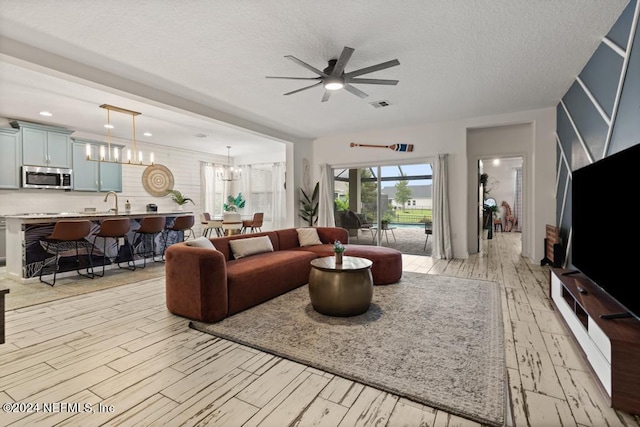 living room with a textured ceiling, light hardwood / wood-style flooring, and ceiling fan with notable chandelier