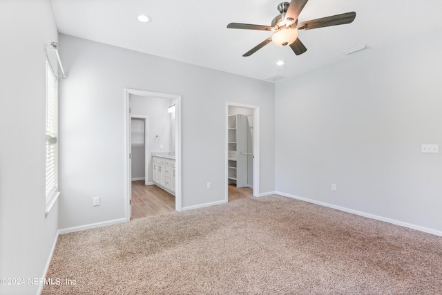 unfurnished bedroom featuring ceiling fan, a closet, a walk in closet, ensuite bathroom, and light colored carpet