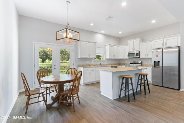 kitchen with light hardwood / wood-style flooring, a kitchen island, appliances with stainless steel finishes, and white cabinetry