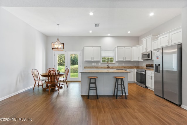 kitchen featuring a kitchen island, white cabinetry, stainless steel appliances, a breakfast bar area, and hardwood / wood-style floors