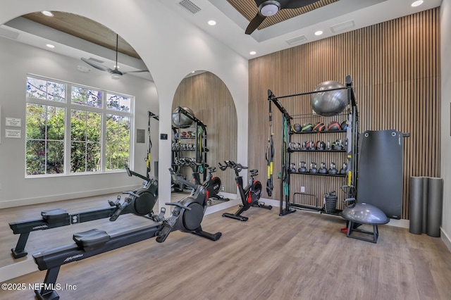 exercise area featuring light wood-type flooring, ceiling fan, and a towering ceiling