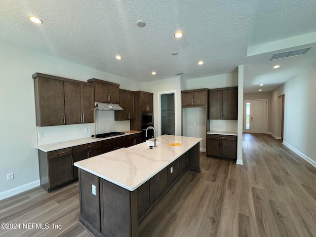 kitchen with dark brown cabinetry, an island with sink, black gas cooktop, and light wood-type flooring