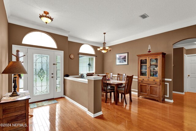 foyer featuring a textured ceiling, ornamental molding, a notable chandelier, and light hardwood / wood-style floors