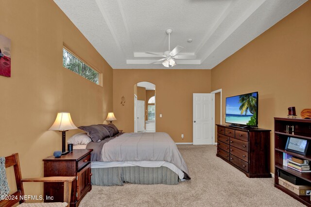 carpeted bedroom with a textured ceiling, a raised ceiling, ceiling fan, and multiple windows