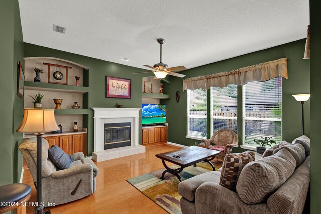 living room with a textured ceiling, light hardwood / wood-style flooring, ceiling fan, and a fireplace