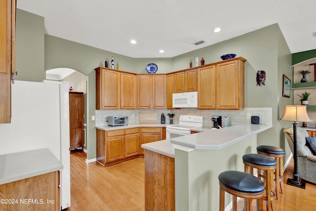 kitchen with kitchen peninsula, white appliances, decorative backsplash, and light hardwood / wood-style floors