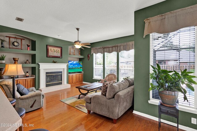 living room with ceiling fan, hardwood / wood-style flooring, a tiled fireplace, and a textured ceiling