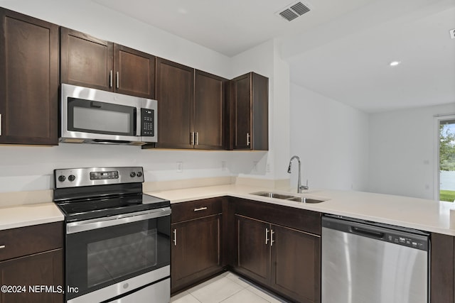 kitchen featuring light tile patterned floors, kitchen peninsula, sink, appliances with stainless steel finishes, and dark brown cabinetry