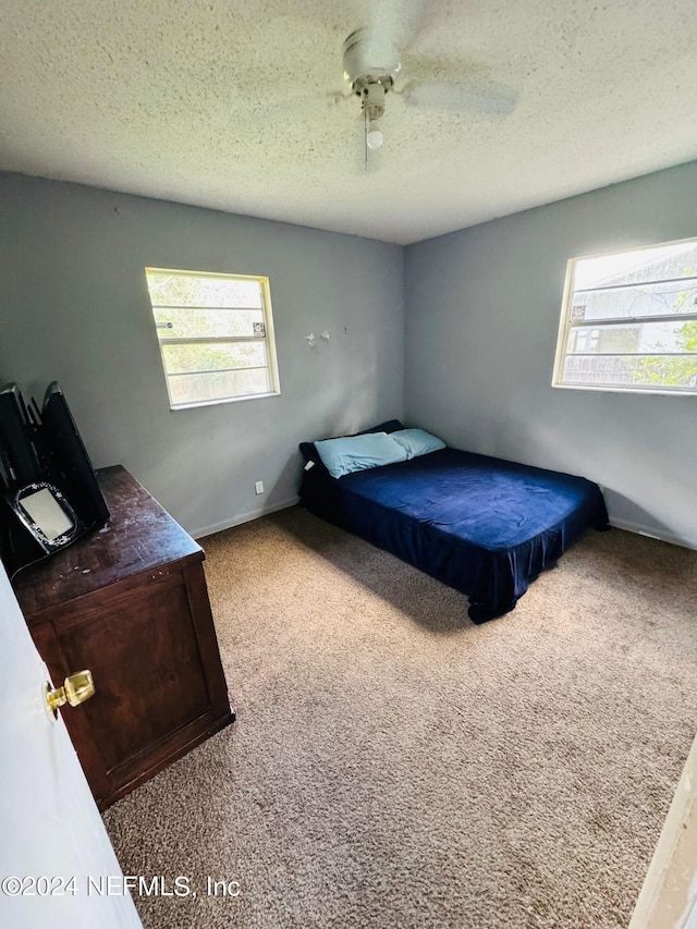 carpeted bedroom featuring ceiling fan and a textured ceiling