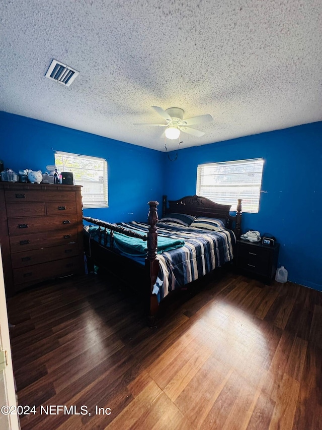 bedroom with a textured ceiling, ceiling fan, and dark hardwood / wood-style flooring