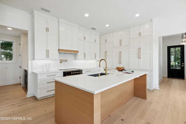 kitchen with an island with sink, a sink, light wood-style flooring, and white cabinets