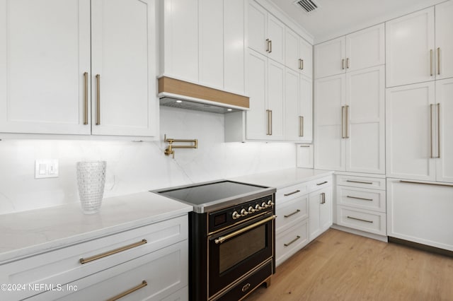 kitchen with high end range, light stone countertops, white cabinetry, premium range hood, and light hardwood / wood-style floors