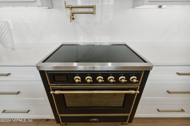 details featuring tasteful backsplash, light countertops, white cabinetry, high end black range, and wood finished floors