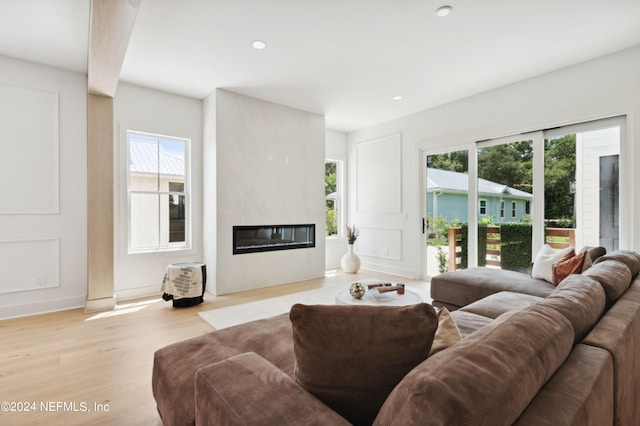 living room with a large fireplace, a healthy amount of sunlight, and light wood-type flooring