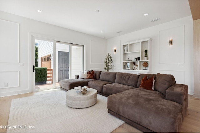 living area with light wood-type flooring, visible vents, a decorative wall, and recessed lighting