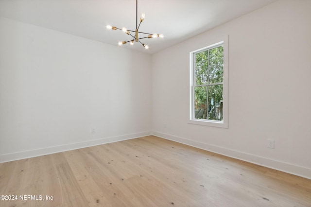 unfurnished room with baseboards, light wood-type flooring, and an inviting chandelier