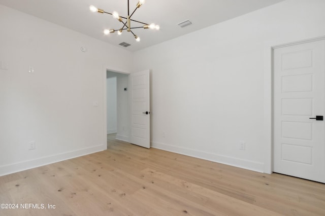 empty room featuring light wood-style flooring, visible vents, and a notable chandelier