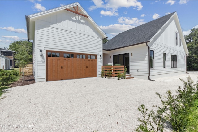 modern farmhouse with driveway, a shingled roof, board and batten siding, and an attached garage