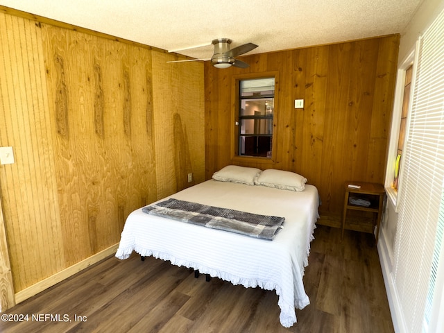 bedroom with a textured ceiling, wood walls, ceiling fan, and dark hardwood / wood-style floors