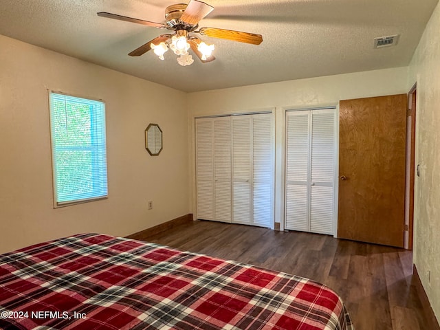 unfurnished bedroom with dark wood-type flooring, two closets, ceiling fan, and a textured ceiling