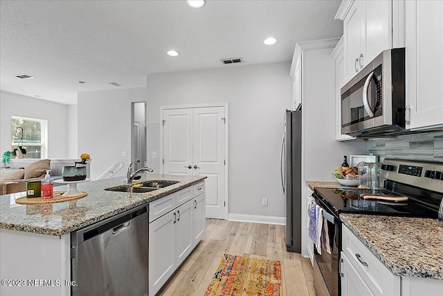 kitchen with light wood-type flooring, sink, appliances with stainless steel finishes, a center island with sink, and white cabinets