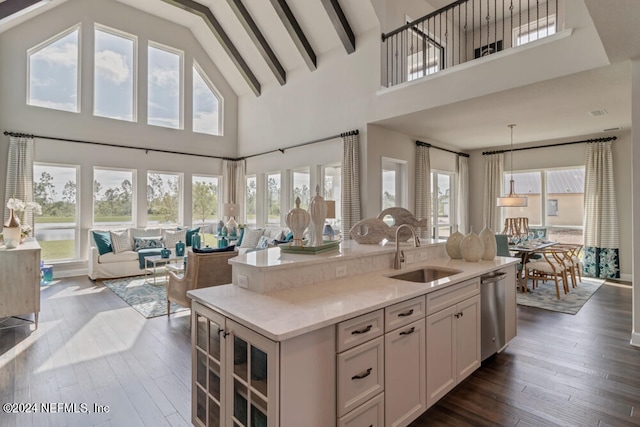 kitchen with high vaulted ceiling, light stone counters, sink, dark wood-type flooring, and a center island with sink