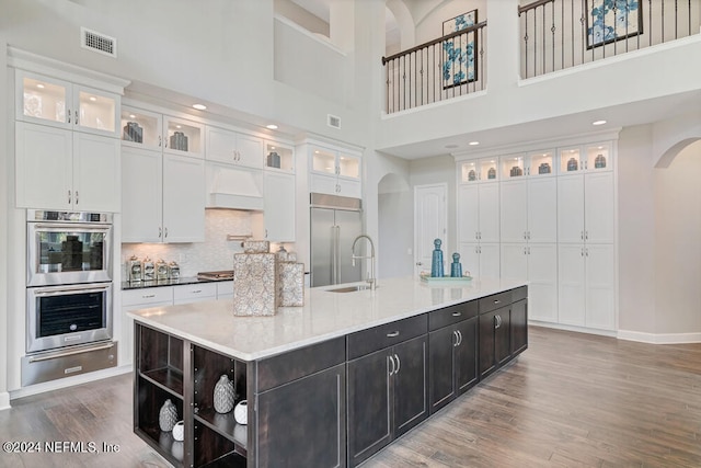 kitchen with a center island with sink, stainless steel appliances, a towering ceiling, and wood-type flooring