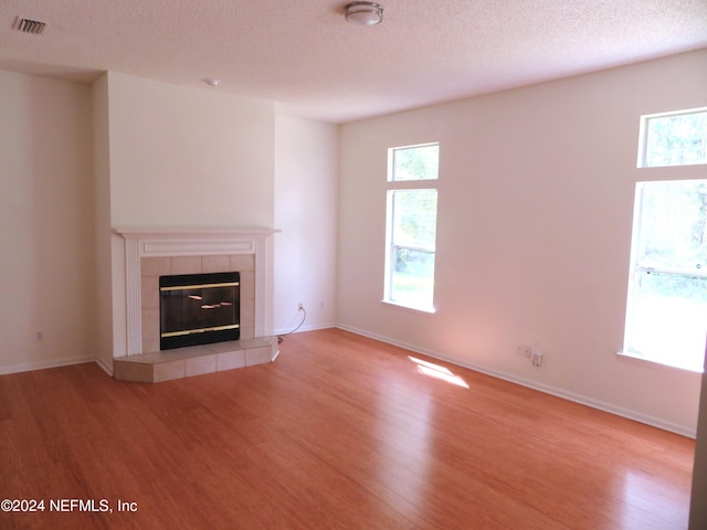 unfurnished living room featuring a textured ceiling, a tile fireplace, and hardwood / wood-style floors